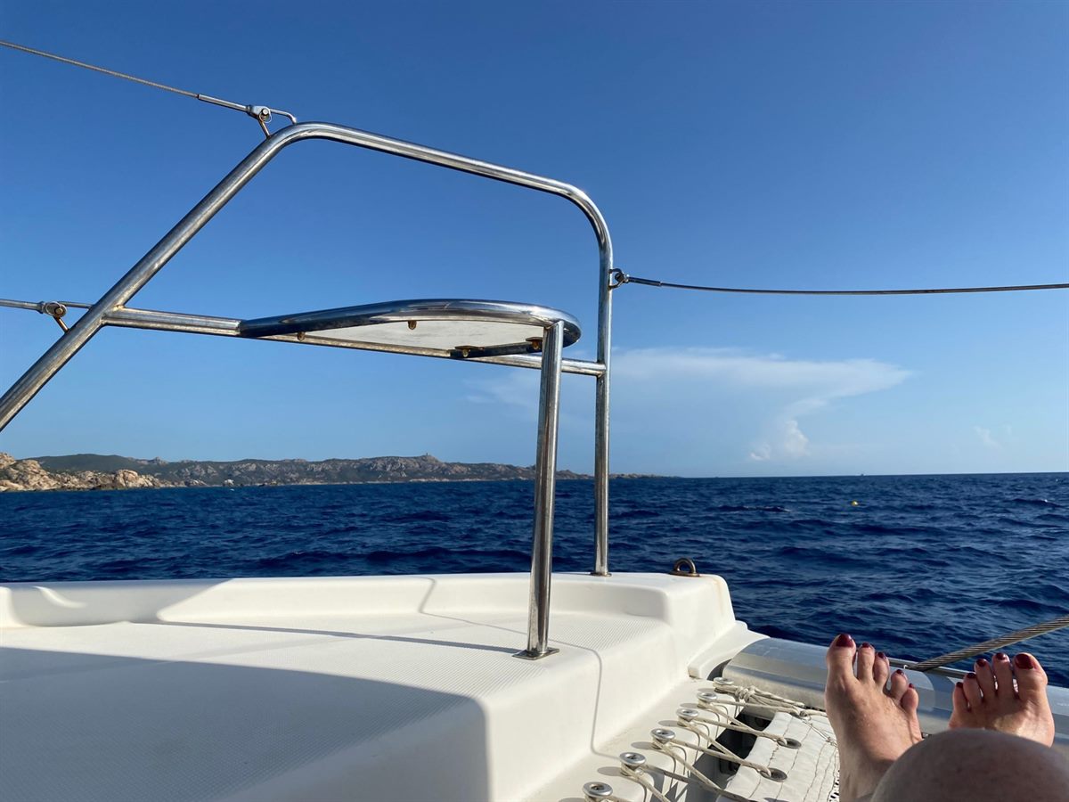 Vue depuis l'avant d'un catamaran, mer bleue et côte rocheuse de Corse à l'horizon