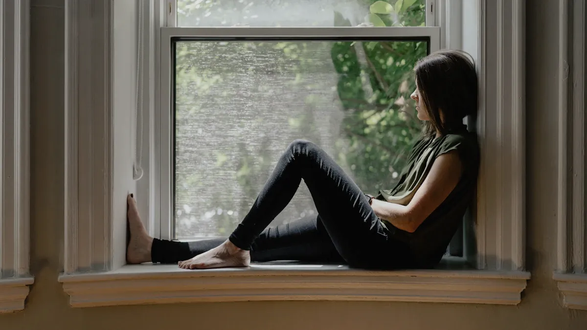 Femme assise sur le rebord d'une fenêtre, le regard tourné vers l'extérieur, en pleine réflexion