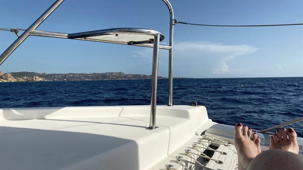 Vue depuis l'avant d'un catamaran, mer bleue et côte rocheuse de Corse à l'horizon