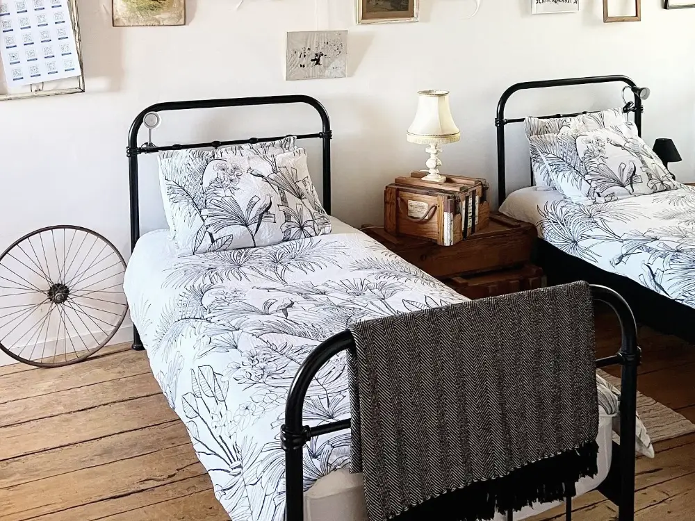 Chambre partagée : deux lits en fer forgé, parquet ancien et lumière naturelle