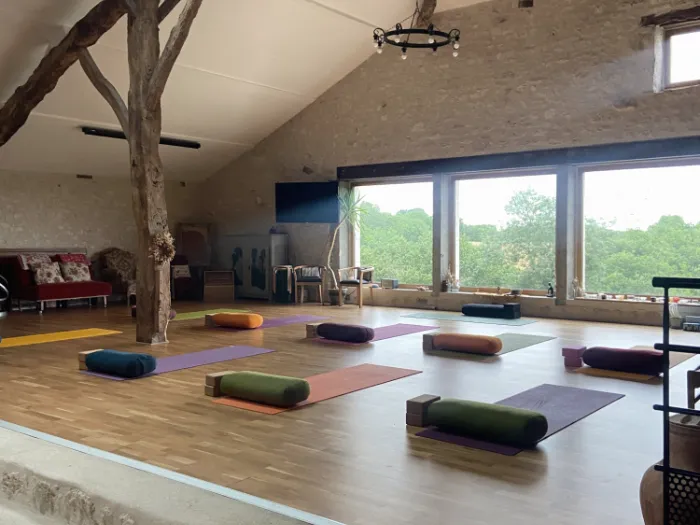 La salle de pratique : tapis, coussins et grandes baies vitrées sur la campagne