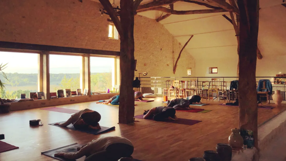 Séance de yoga dans la grande salle de The Happy Hamlet, baignée de lumière, face à la campagne