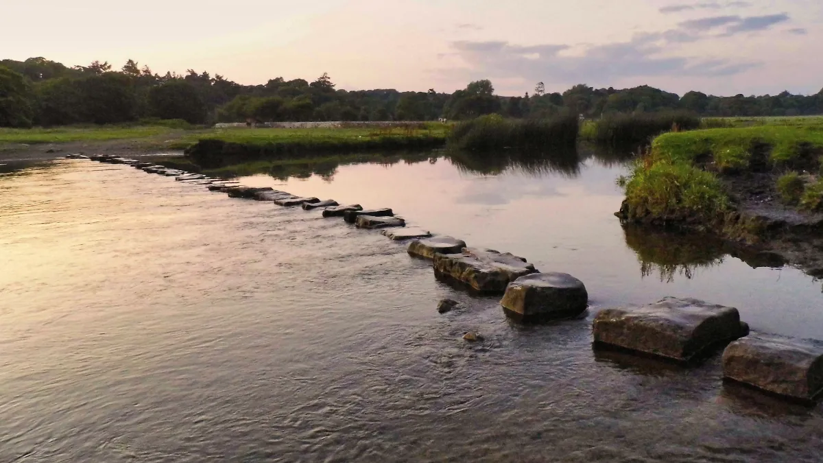Pierres de gué traversant une rivière calme au coucher du soleil, image d'une reconversion menée pas à pas