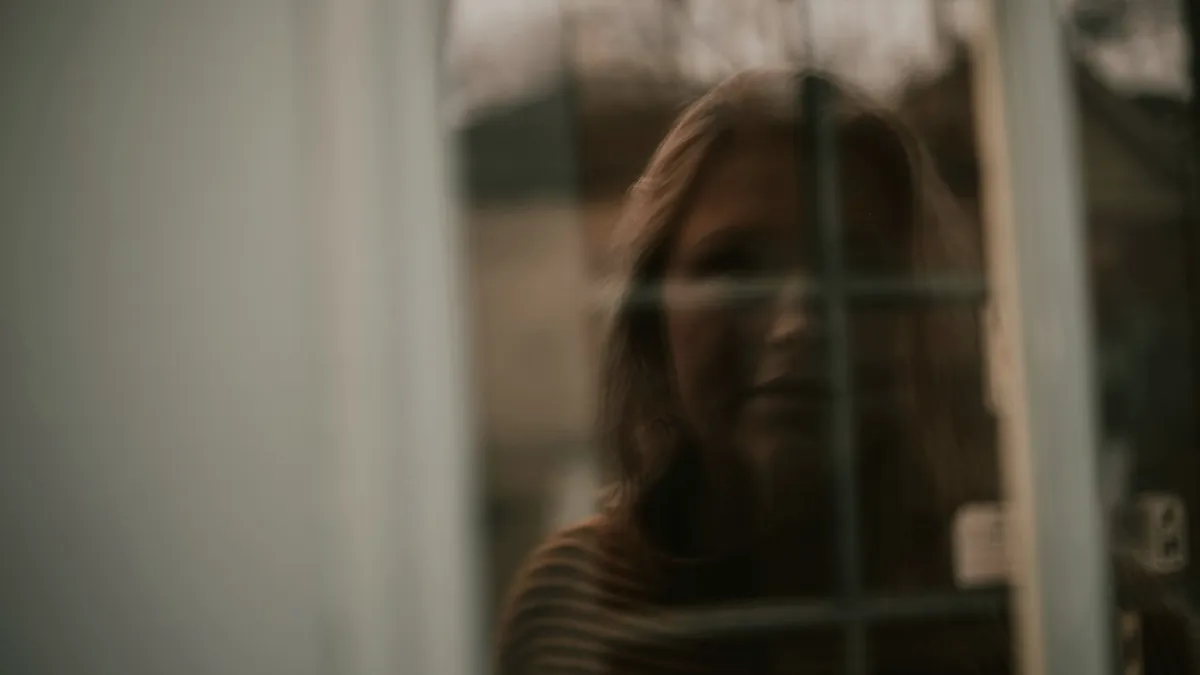 Reflet flou d'une femme dans une vitre, le visage à demi effacé par le cadre de la fenêtre