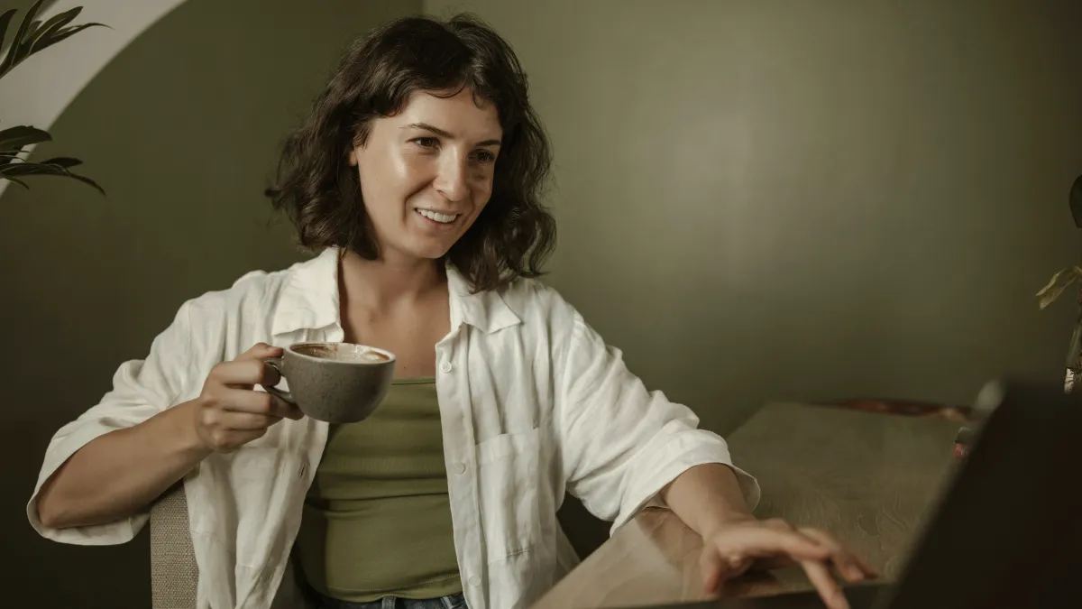 Femme souriante, une tasse à la main, en séance de coaching en visio depuis chez elle